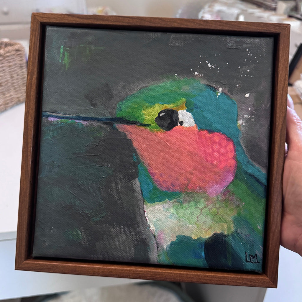 a hand holds a framed hummingbird painting