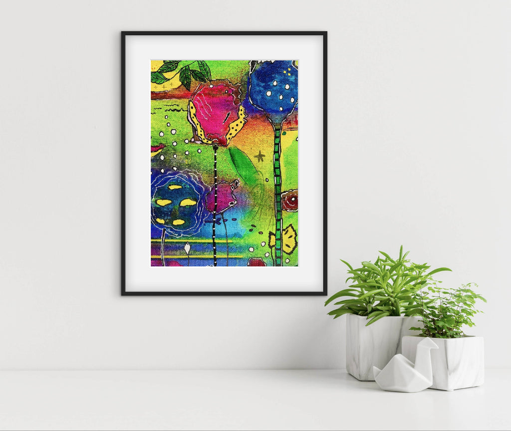 Framed colorful abstract art print on a white wall with plants below.