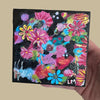 abstract floral painting on a wood block held by a hand in front of a beige background