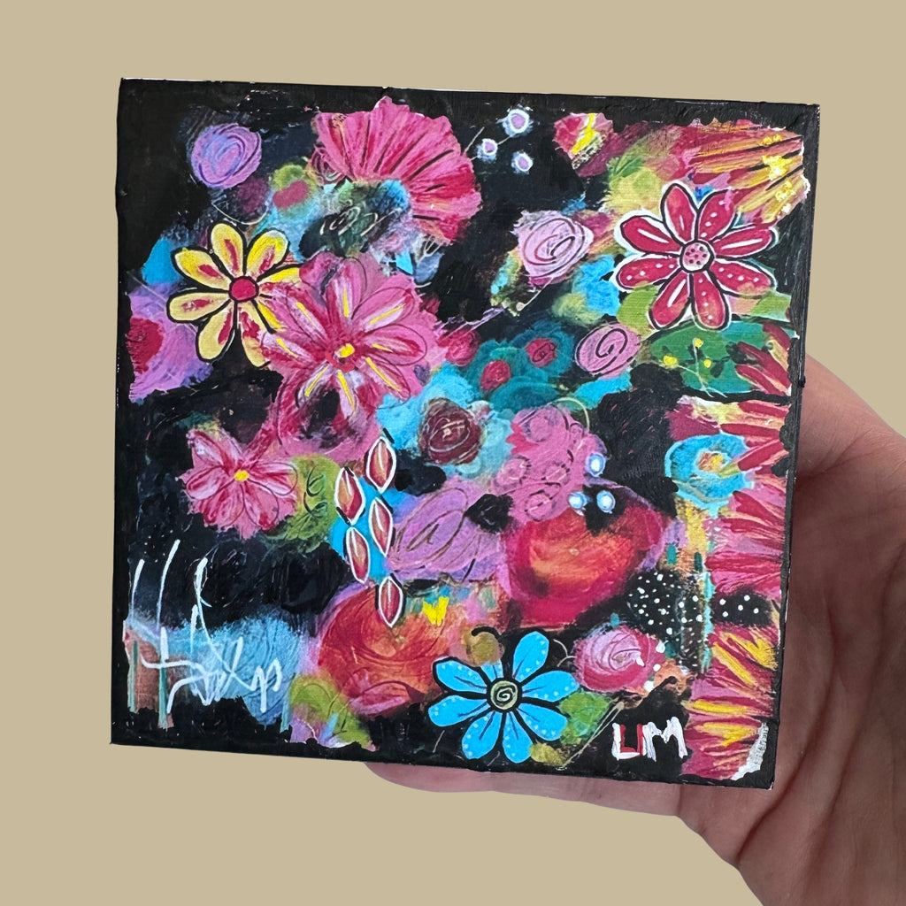 abstract floral painting on a wood block held by a hand in front of a beige background