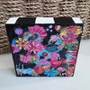painted wood block that is square and has black and white stripes on the top. It is displayed on a table with a basket