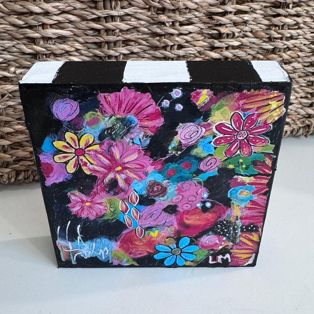 painted wood block that is square and has black and white stripes on the top. It is displayed on a table with a basket