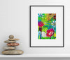 Framed colorful floral artwork on a white wall with stacked stones below.