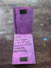 A handmade purple and lavender paper art piece with black magnetic closures, featuring handwritten text that reads 'original art Created using recycled Materials' displayed on a rustic wooden background.