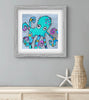 Framed artwork of a colorful octopus on a gray wall with a vase and starfish below.