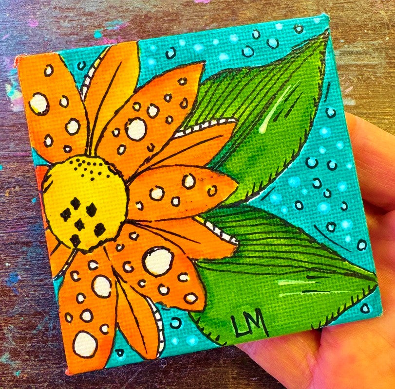 A hand holding a small square canvas painting featuring a orange flower with a yellow center, green leaves, and a turquoise background.