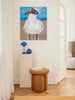 Painting of a bird with sunglasses on a wall above a white pedestal with decorative items.