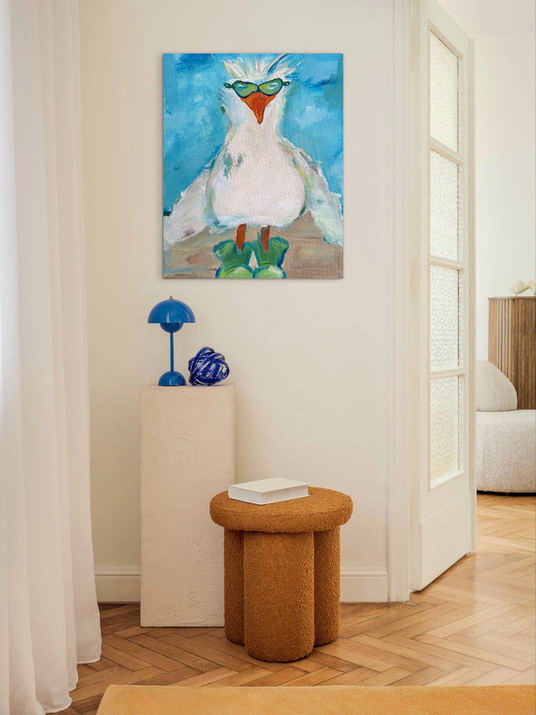 Room interior with a colorful bird painting on the wall, a brown stool, and decorative items.