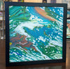 abstract painting in a black frame sitting on a table