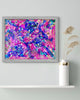 Framed abstract artwork with pink and blue colors on a white wall.