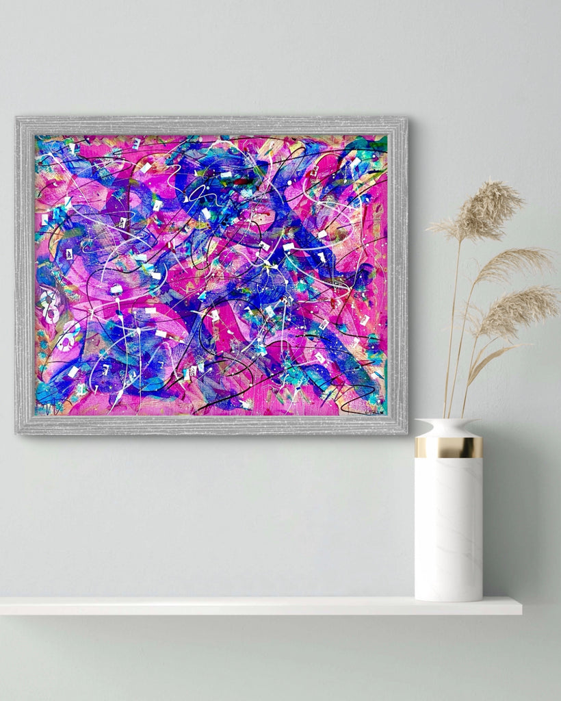 Framed abstract artwork with pink and blue colors on a white wall.