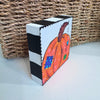 pumpkin art on a wood block sitting on a white table in front of a basket
