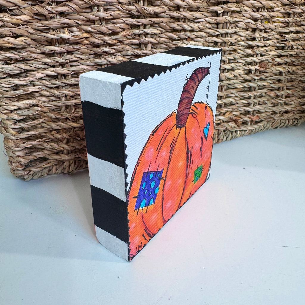 pumpkin art on a wood block sitting on a white table in front of a basket