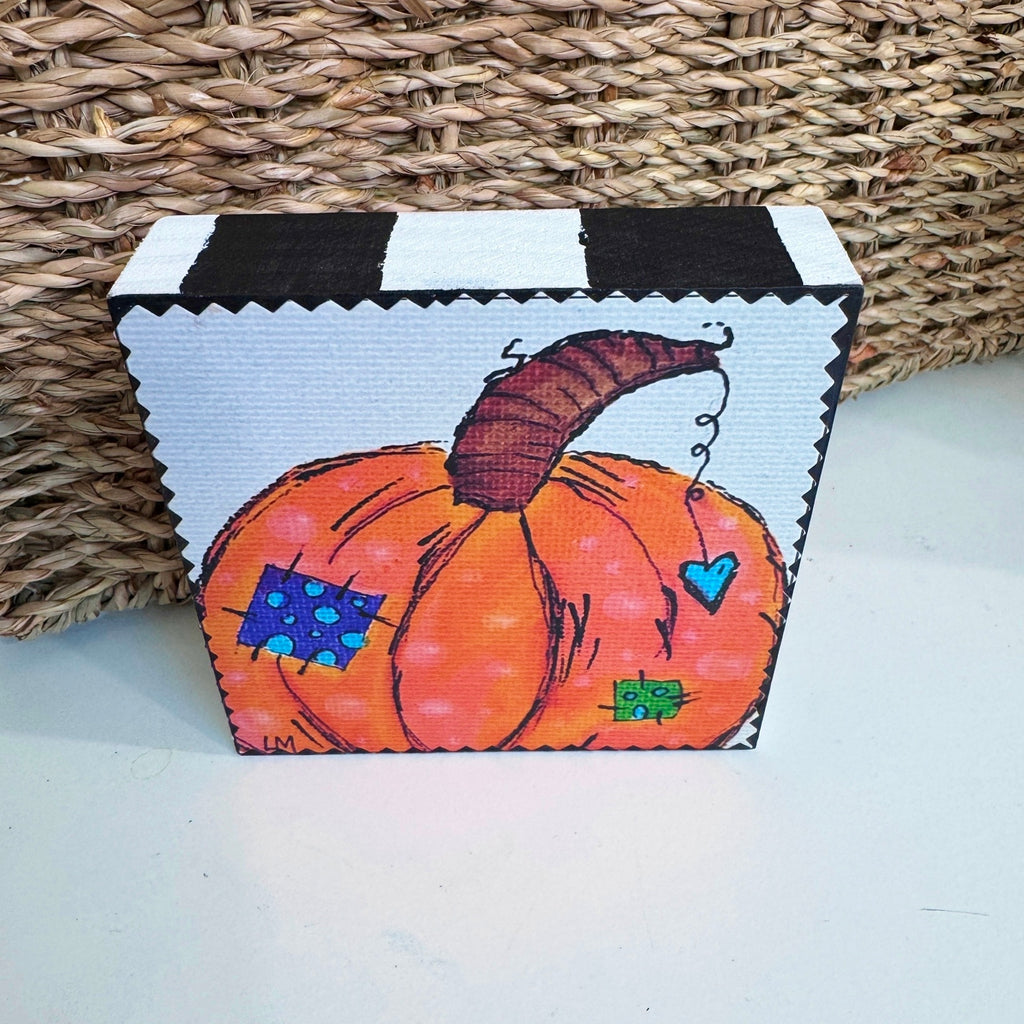 pumpkin art on a wood block sitting on a white table in front of a basket