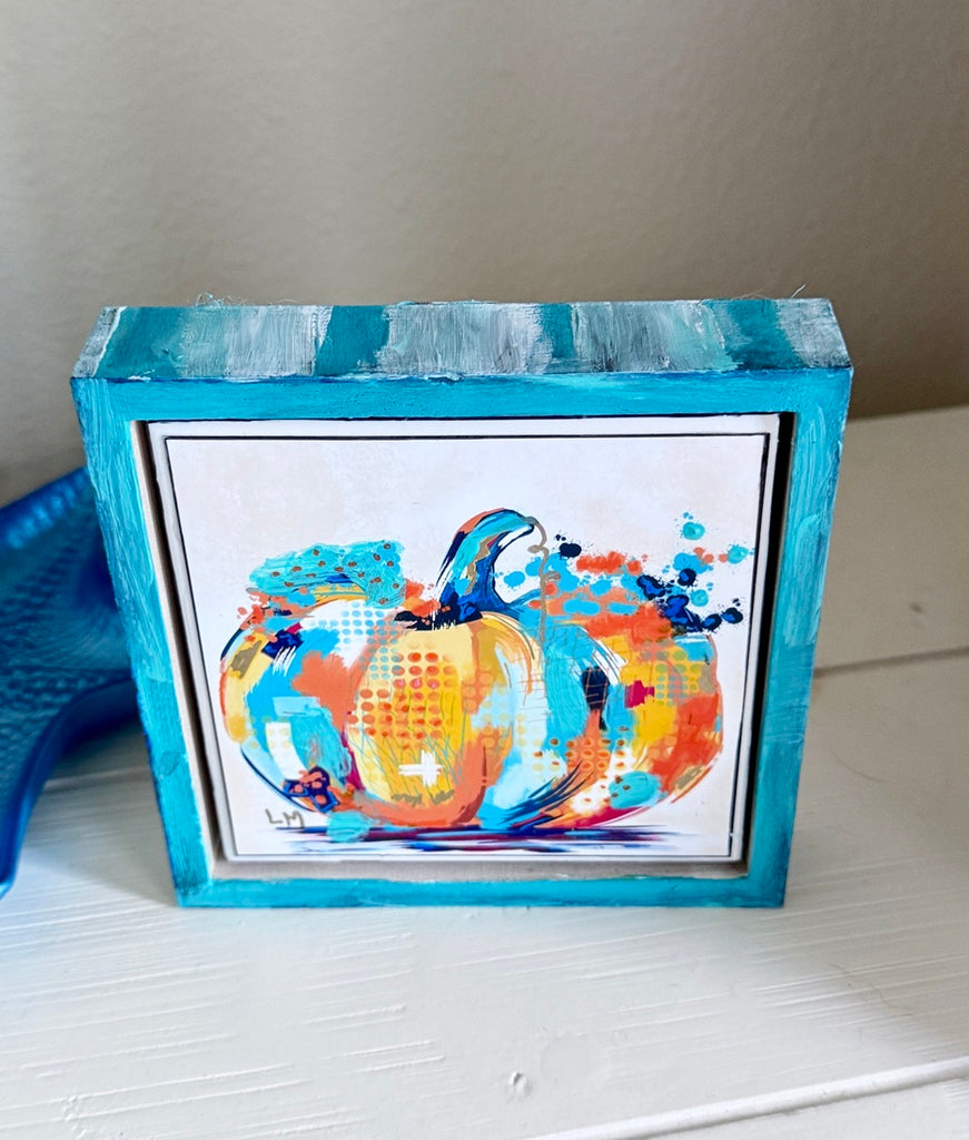 pumpkin artwork in a painted frame on a table next to a trinket dish