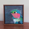 a framed hummingbird painting on a brown table against a white wall