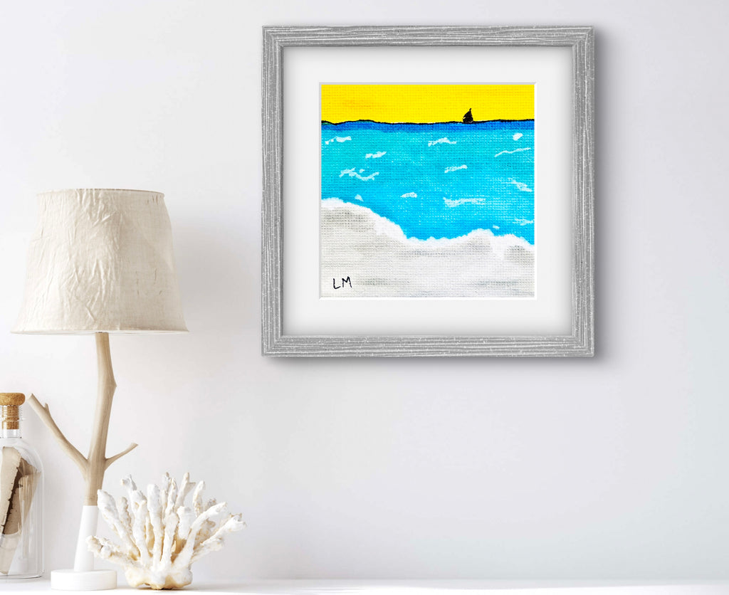 Framed artwork of a beach scene with blue water and yellow sky on a white wall.