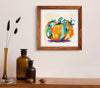Framed abstract pumpkin painting on a wall above a wooden shelf with decorative items.