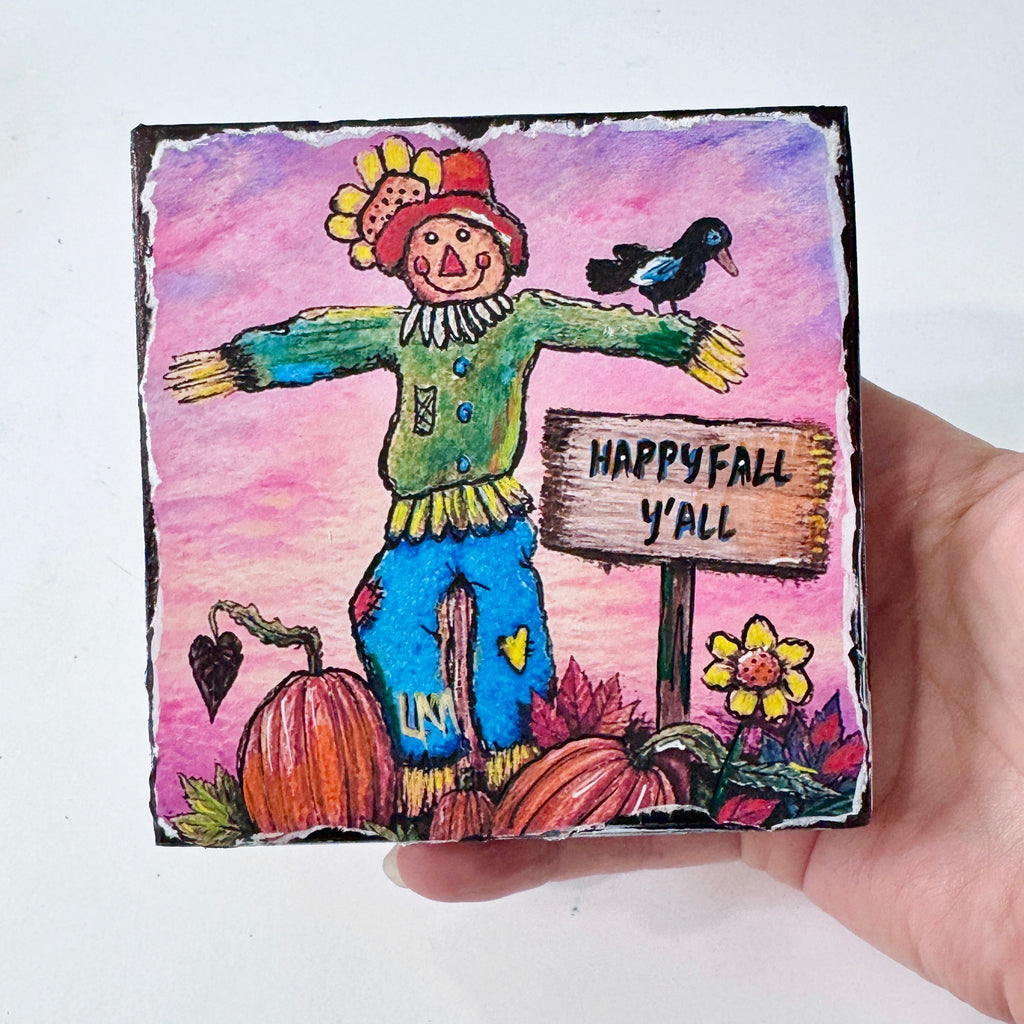 whimsical scarecrow artwork held by a hand. A sign on the art says "happy Fall Y'all". Scarecrow is in a pumpkin patch with a crow, pumpkins and flowers