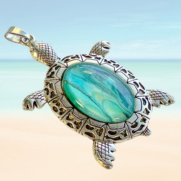 Turtle-shaped pendant with turquoise art glass on a beach background