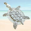 Back of a silver turtle pendant with honeycomb pattern on a beach background