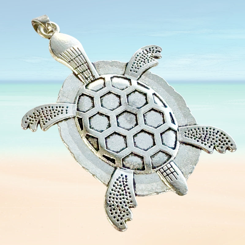 Back of a silver turtle pendant with honeycomb pattern on a beach background