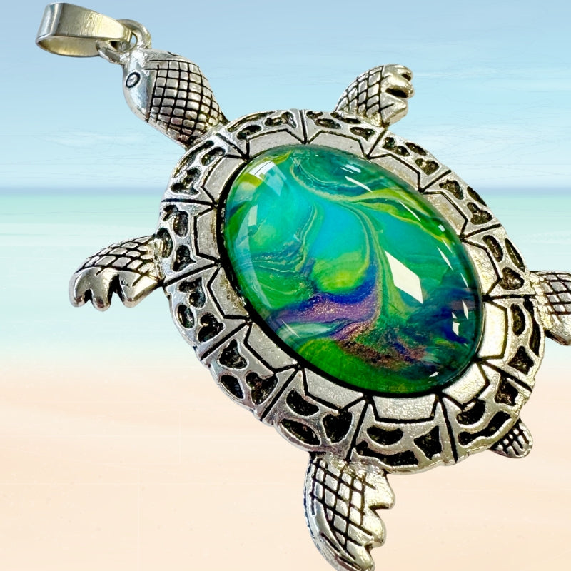 turtle shaped pendant with a green and blue glass stone against a beach background