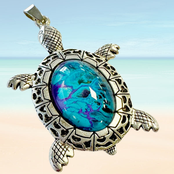 Turtle-shaped pendant with a blue stone on a beach background