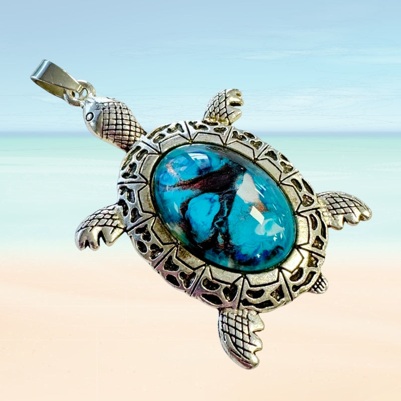 Turtle shaped pendant with turquoise glass center on a gradient background