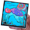 a sea turtle painting being held by a hand with a white background