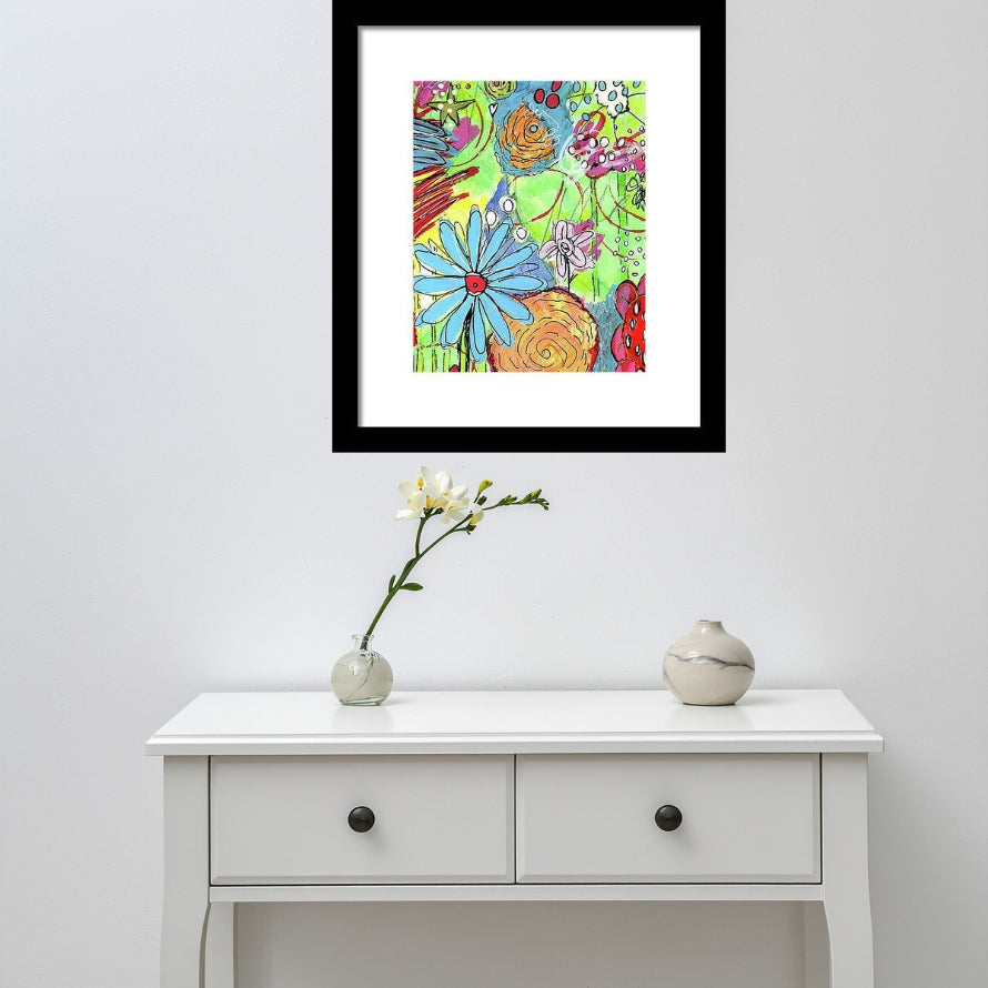 A framed colorful floral art print hangs on a light gray wall above a white console table with two small decorative vases and a single white flower.
