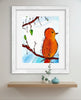 Framed artwork of a bird on a branch with a white frame, displayed on a wall above a shelf.