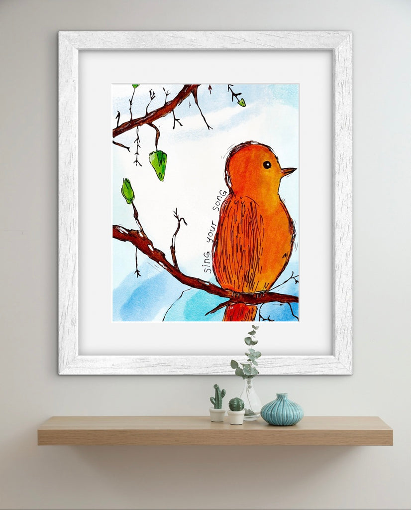 Framed artwork of a bird on a branch with a white frame, displayed on a wall above a shelf.