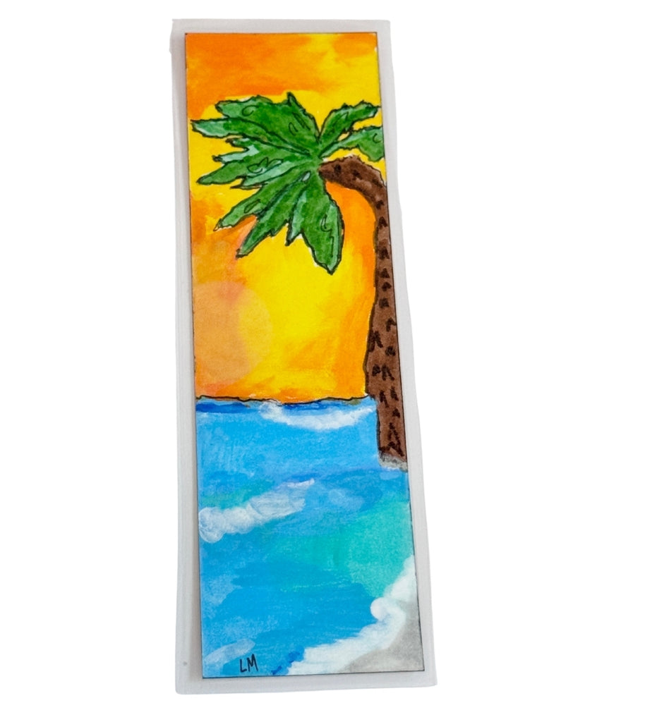 beach scene painted on a laminated bookmark with a sunset sky and a palm tree, Initials for the artist 'LM' on lower corner