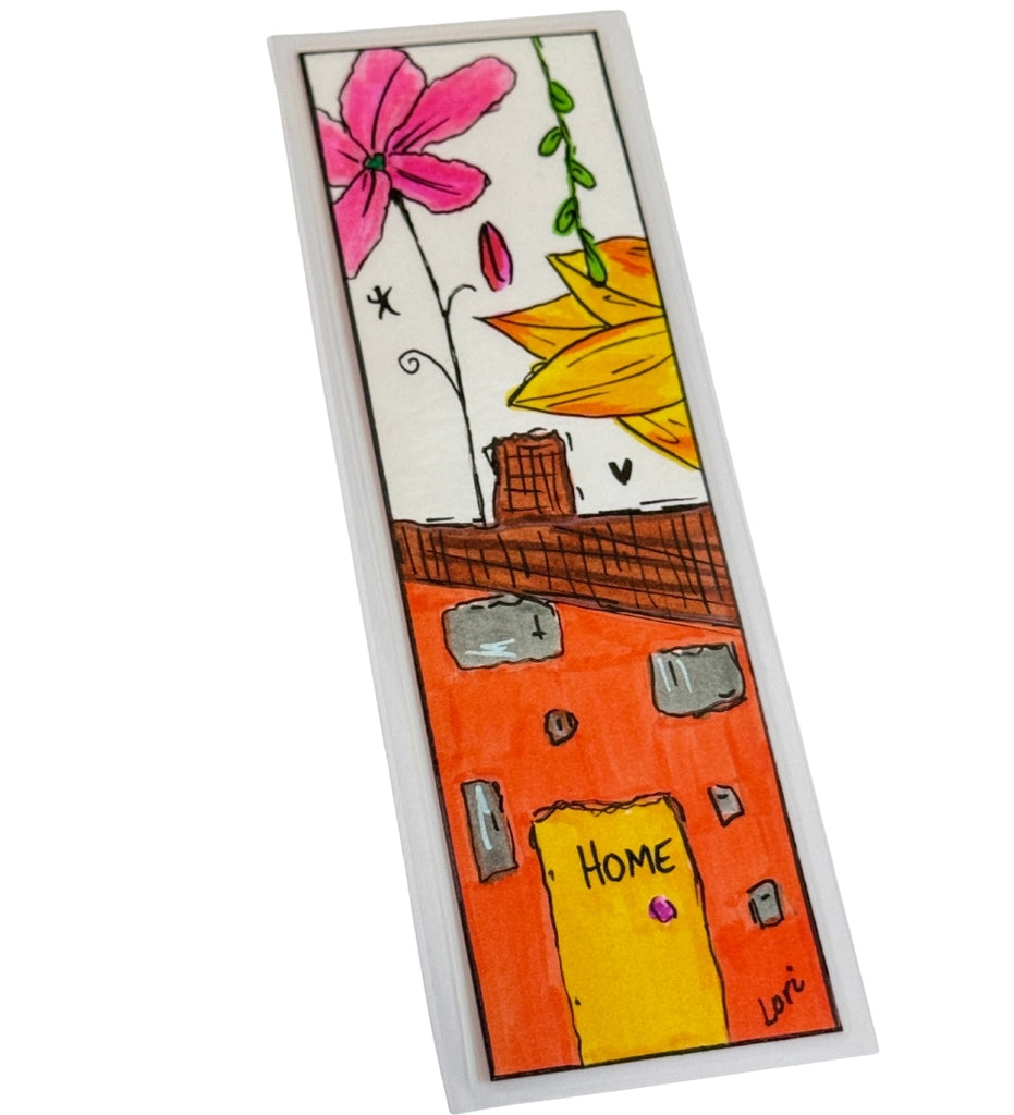 A rectangular bookmark featuring a colorful hand-painted illustration of a house with a yellow door labeled 'HOME', gray windows, a brown roof, a pink flower, and a yellow leaf on a white background.