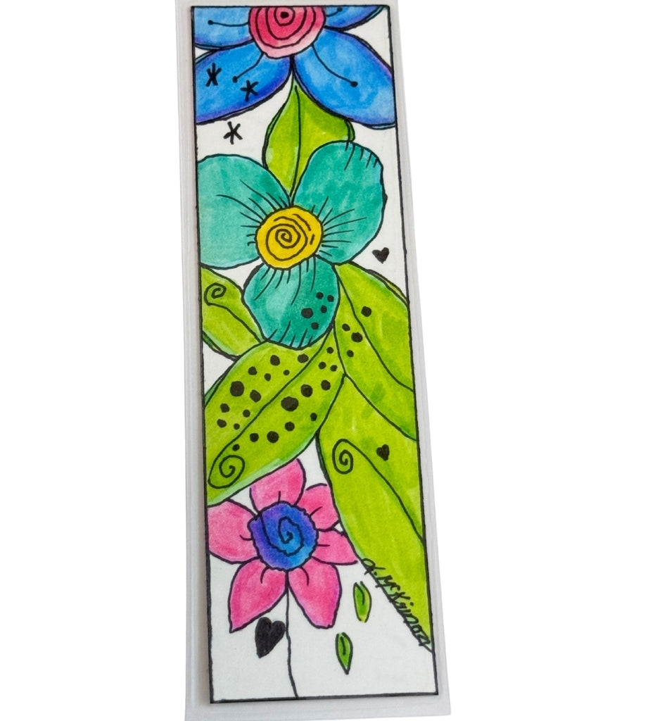 A rectangle bookmark featuring a colorful hand-drawn floral design with blue, teal, pink, and green flowers, black outlines, and small decorative marks. The item is photographed against a plain white background. Signed by artist 