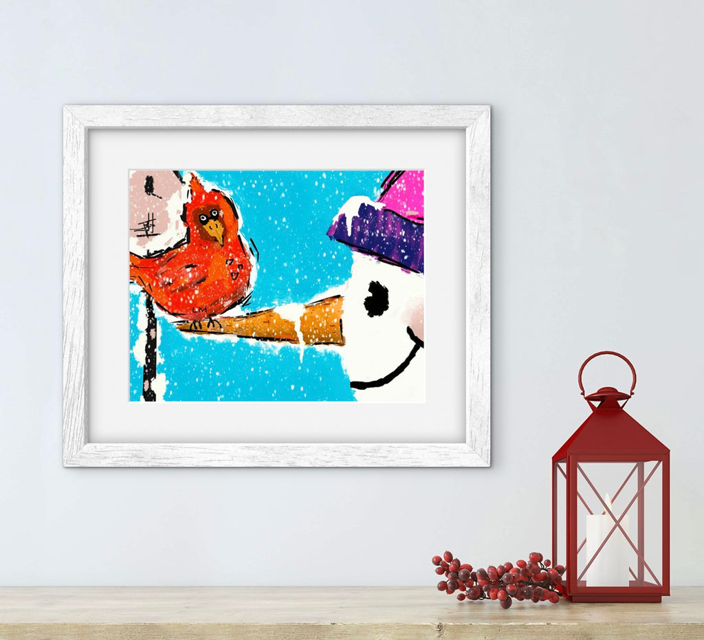 Framed artwork of a bird and snowman on a light blue background, with a red lantern and decorative branches on a wooden surface.