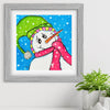 Framed artwork of a colorful snowman on a white wall with a plant in the corner.