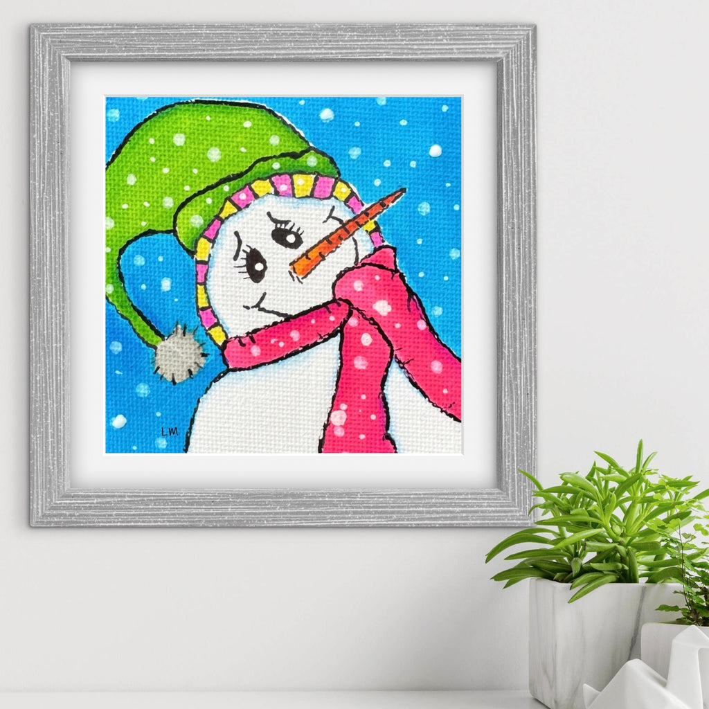 Framed artwork of a colorful snowman on a white wall with a plant in the corner.