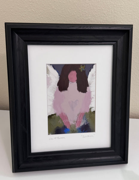 an angelic art print in a black frame with a white mat sitting on a white table 