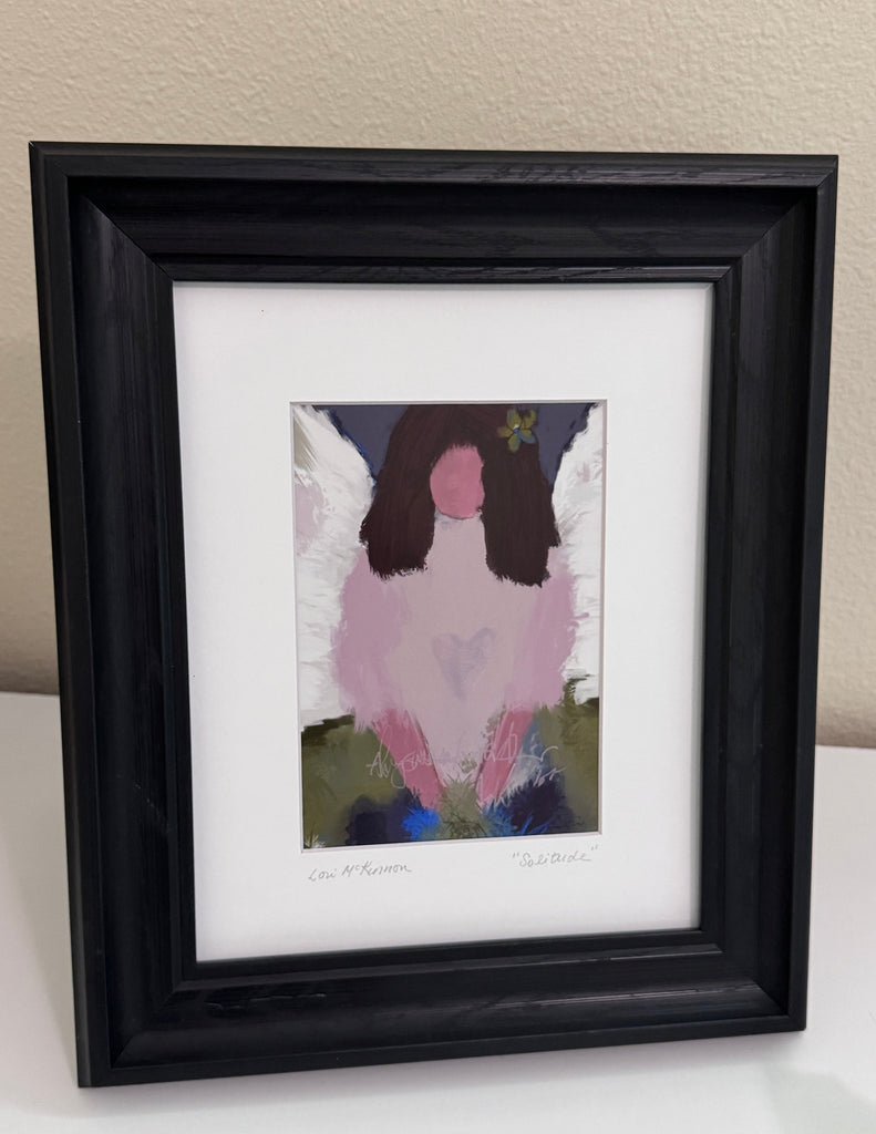 an angelic art print in a black frame with a white mat sitting on a white table 