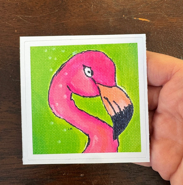 Hand holding a sticker with a pink flamingo on a green background