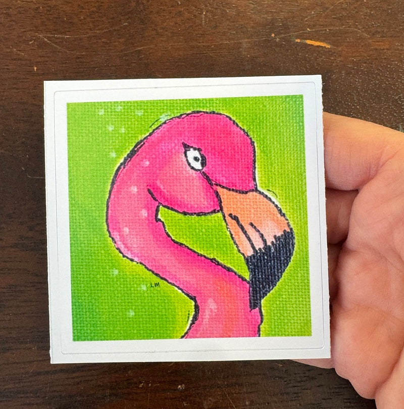 Hand holding a sticker with a pink flamingo on a green background