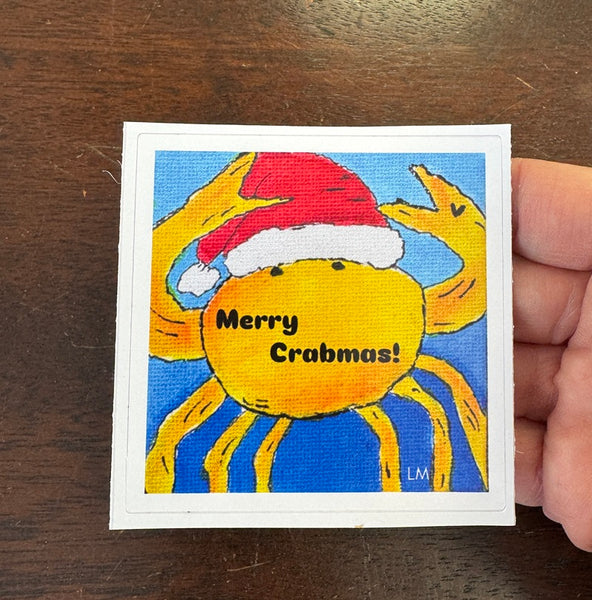 Sticker featuring a crab wearing a Santa hat and 'Merry Crabmas!' text on a wooden surface.
