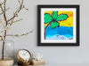 Framed artwork of a palm tree and beach scene on a wall with decorative items below.