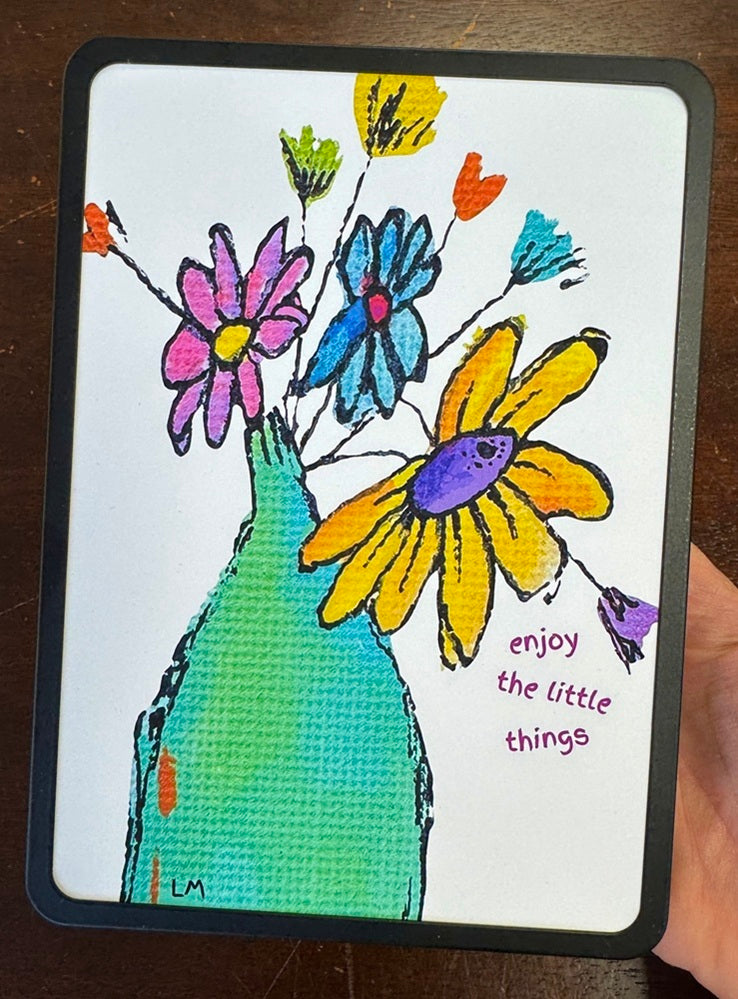 Art print in a black frame with flowers in a green bottle and 'enjoy the little things' text. 