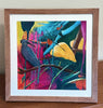 colorful tropical painting with leaves, branches and a bird in a brown frame sitting on a desk