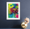 Framed colorful abstract art piece on a dark blue wall with a decorative vase.