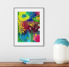 Colorful abstract art print on a white wall above a wooden shelf with books and a vase.