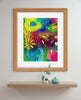 Framed colorful abstract painting on a wall above a shelf with decorative items.